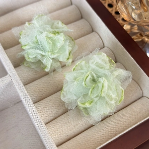 Macro view of light green mesh fabric flower stud earrings on a beige jewelry display