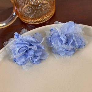Detail of blue mesh flower earrings on a ceramic plate with warm aesthetic lighting
