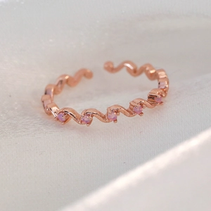 Macro shot of adjustable rose gold wave ring featuring five round pink gemstones on silk