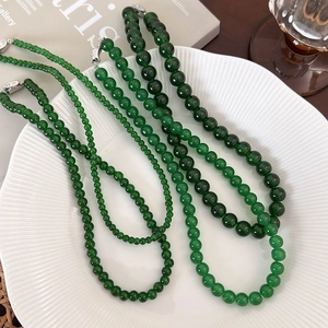 Elegant green bead necklaces with silver lobster clasps displayed on a white ceramic plate