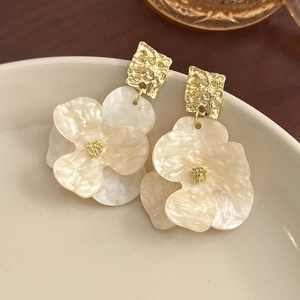 Detail of cream acrylic flower earrings with textured gold square studs on a ceramic tray