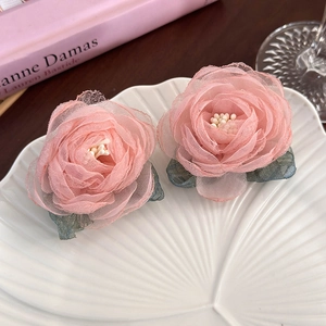 Detailed close-up of pink mesh rose earrings with green lace leaves on white shell plate