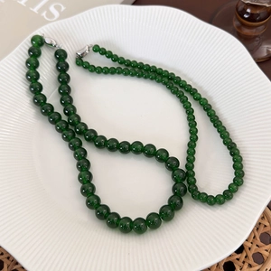 Macro shot of deep green beaded necklace with silver clasp on white ceramic tray