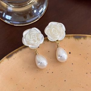 Macro di eleganti orecchini a rosa con pendenti di perle su un vassoio di ceramica