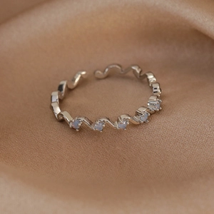 Detailed close-up of wavy silver open ring with opal-like stones on silk fabric