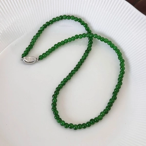 Detail of green beaded necklace with silver oval clasp on white porcelain tray