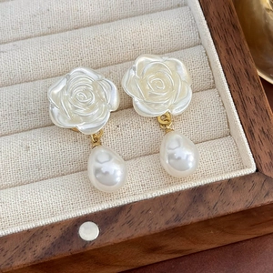 Dettaglio di orecchini a rosa bianca con perle a goccia e accenti in metallo oro