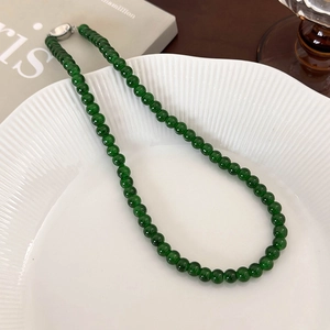 Close-up of emerald green beaded necklace with silver buckle on a white textured plate
