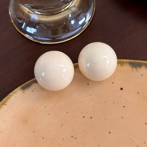 Macro di orecchini a sfera color crema lisci su un piatto decorativo in ceramica