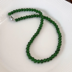 Close-up of deep green beaded necklace with silver buckle on a white textured plate