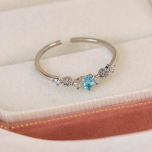 Macro view of heart-shaped blue zircon ring with opal accents on beige velvet