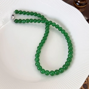 Close-up of green beaded necklace with silver buckle on a textured white ceramic plate