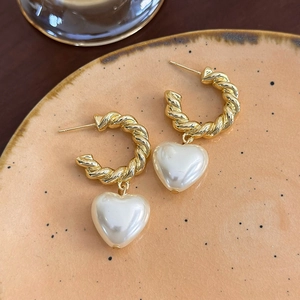 Dettaglio degli orecchini a cerchio dorati ritorti con pendenti a cuore bianchi