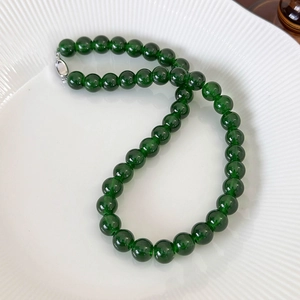 Macro detail of deep green beaded necklace with high luster and silver metal clasp