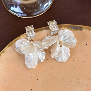 Dettaglio di orecchini a petalo bianco con ganci dorati e cristalli scintillanti