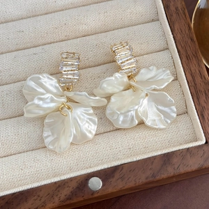 Dettaglio di orecchini a petalo bianco con strass su un portagioie in velluto beige