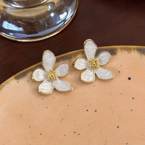 Dettaglio orecchini a fiore con petali bianchi e bordi dorati su piatto in ceramica
