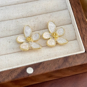 Primo piano di eleganti orecchini a fiore con petali bianchi e dettagli dorati su base in legno