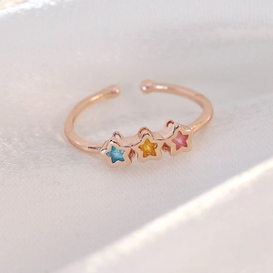 Detailed close-up of rose gold star ring with colorful glitter inlay on white silk