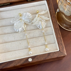 Dettaglio degli orecchini a petalo con perle e nappe dorate in una scatola