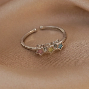 Macro detail of silver adjustable ring with three colorful star-shaped stones on silk fabric