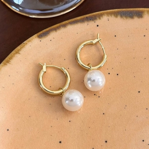 Dettaglio ravvicinato di orecchini a cerchio dorati con perle bianche su piatto ceramico