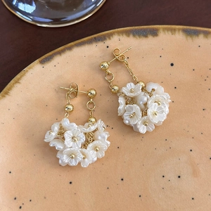 Dettaglio degli orecchini pendenti con fiori bianchi e catena dorata su piatto in ceramica