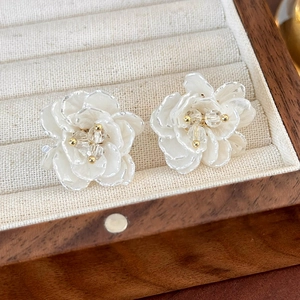 Dettaglio di orecchini a fiore bianco con perle e diamanti su portagioie in legno
