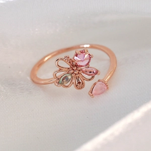 Macro detail of rose gold floral ring with pink crystals on white silk background