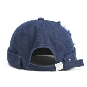 Détail du bonnet docker en denim bleu foncé avec trou usé et boucle en métal argenté