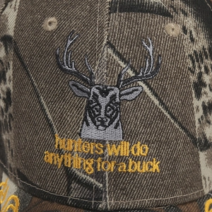 Close-up of deer head and 'hunters will do anything for a buck' embroidery on camo cap