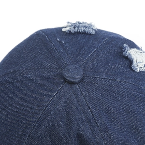 Détail de la casquette en jean vieilli montrant le bouton et la structure à six panneaux