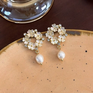 Dettaglio di orecchini a petalo bianco con strass e perle a goccia su un vassoio di ceramica