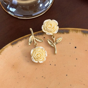 Dettaglio di orecchini a rosa giallo crema con steli dorati su un piatto vintage
