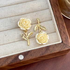 Dettaglio macro di orecchini a rosa asimmetrici con petali crema e foglie d'oro lucido