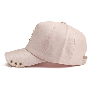 Detail of light pink baseball cap featuring three gold metal rings on the brim and rivets