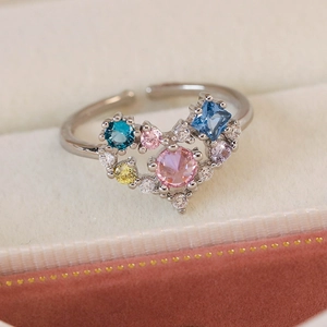 Detail of adjustable ring featuring a multi-colored zircon heart on beige velvet