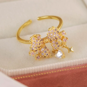 Detail of gold bow ring with pink pavé stones and heart star charms in a gift box