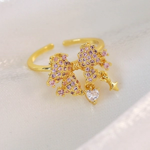 Macro detail of adjustable gold ring featuring pink pavé bow and hanging heart zircon
