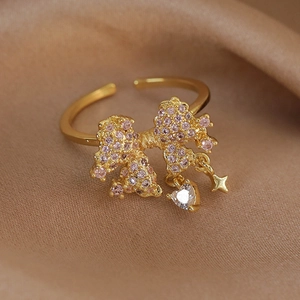 Detail shot of golden bow ring with pink cubic zirconia and dangling star heart charms