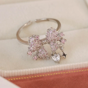 Detailed close-up of a bow ring with pink zircon and dangling heart star pendants