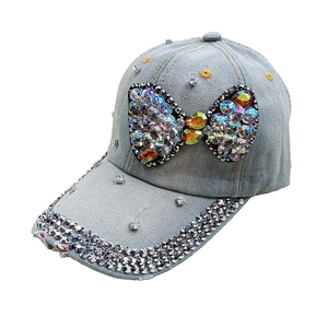Detail of light blue denim baseball cap featuring colorful rhinestone bow and brim