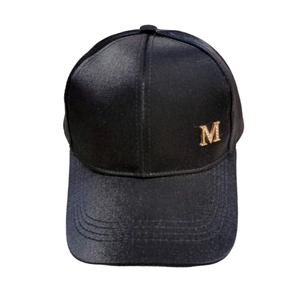 Detailed close-up of glossy black satin baseball cap with gold metal M letter decoration
