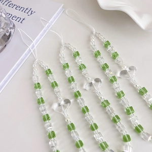 Détail de perles carrées vertes et breloque coeur transparent sur une dragonne de téléphone