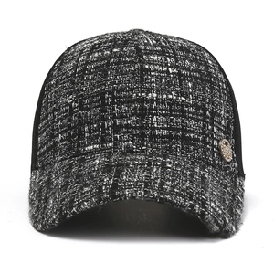 Close-up of black and white tweed baseball cap with a gold emblem and textured weave