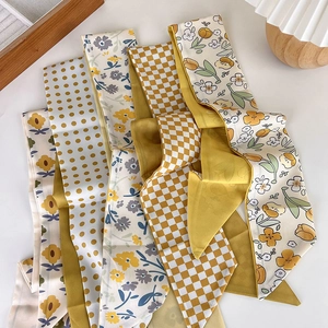 Collection of yellow silk scarves with polka dot and floral prints on a white table