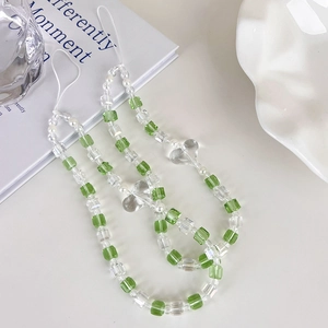 Dragonne de téléphone perlée verte et blanche avec breloques cœur sur un décor épuré