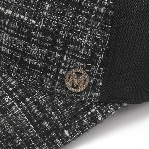 Close-up of black and white tweed fabric with a gold rhinestone M logo on the cap side