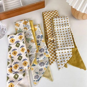 Close-up of assorted yellow Twilly silk scarves with floral, checkered, and polka dot patterns