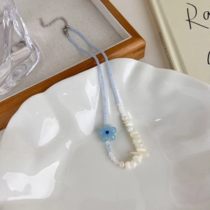 Détail d'un collier de perles avec fleur bleue et perles sur une assiette en céramique